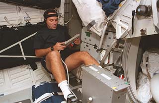 STS-79 mission specialist Carl Walz, wearing a headband and earphones, adjusts the controls on the ergometer as he exercises on the Atlantis's middeck. 